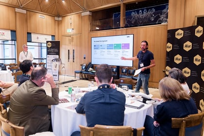 Darryl Kennedy talks through a slide presentation in front of a group of people sitting around tables